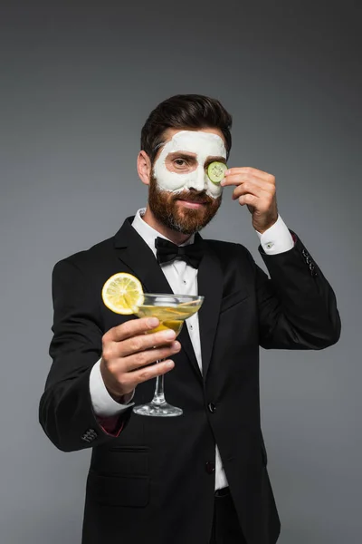 Happy man in suit with clay mask on face holding cocktail isolated on grey — Stockfoto