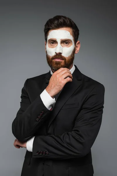 Portrait of bearded man in suit with clay mask on face isolated on grey — Stock Photo