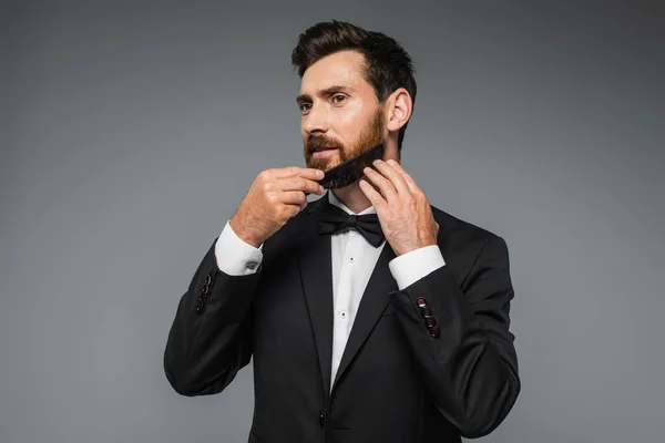 Man in tuxedo brushing beard with comb isolated on grey — Foto stock