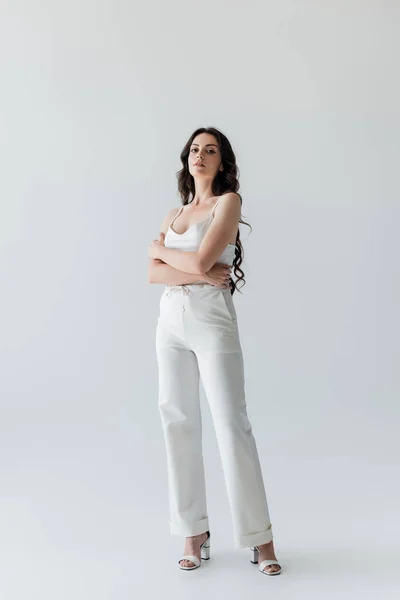 Full length of stylish model in white clothes looking at camera on grey background — Foto stock