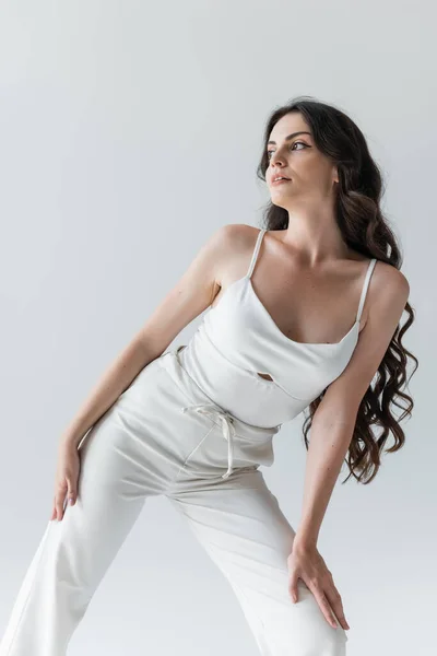 Красива брюнетка в білому одязі позує ізольовано на сірому — стокове фото