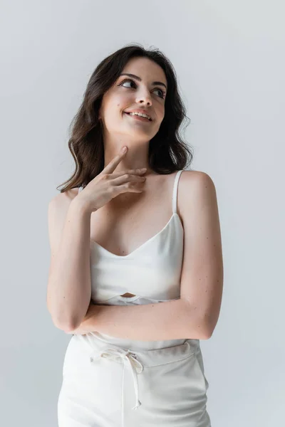 Dreamy woman in white clothes looking away and touching neck isolated on grey — Stock Photo