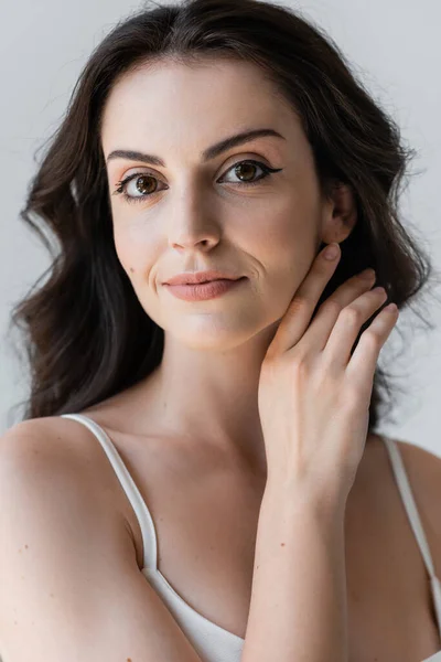 Portrait of young model with makeup touching face isolated on grey — Stockfoto