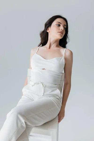 Stylish woman in white clothes sitting on chair isolated on grey — Stock Photo