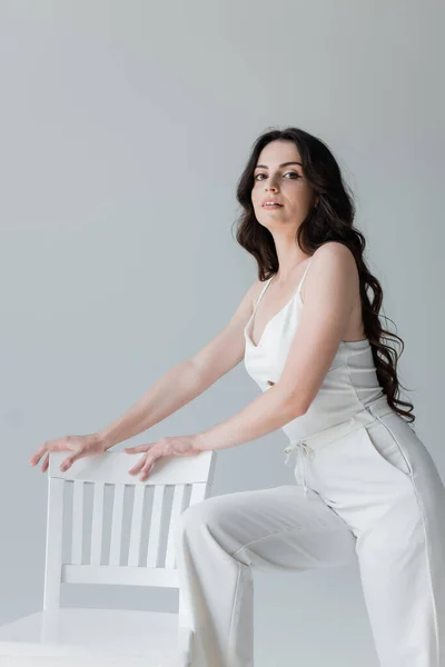 Long haired brunette model standing near chair isolated on grey — Stockfoto