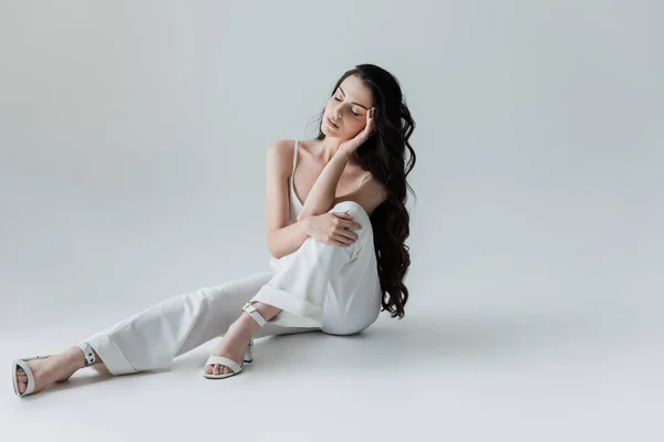 Stylish woman in white clothes sitting on grey background — Photo de stock