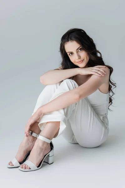 Full length of stylish model in heels and while clothes looking at camera on grey background — Stock Photo