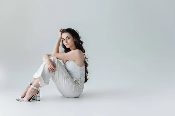Young woman in heels and white clothes looking at camera on grey background — Foto stock