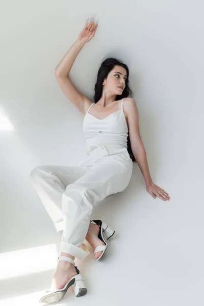 Модна модель в білому одязі позує на сірому фоні з сонячним світлом — стокове фото