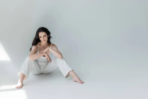 Barefoot woman in white clothes looking at sunlight on grey background — Stock Photo