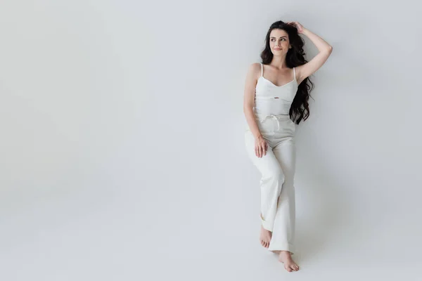 Full length of barefoot woman in white clothes smiling on grey background — Foto stock