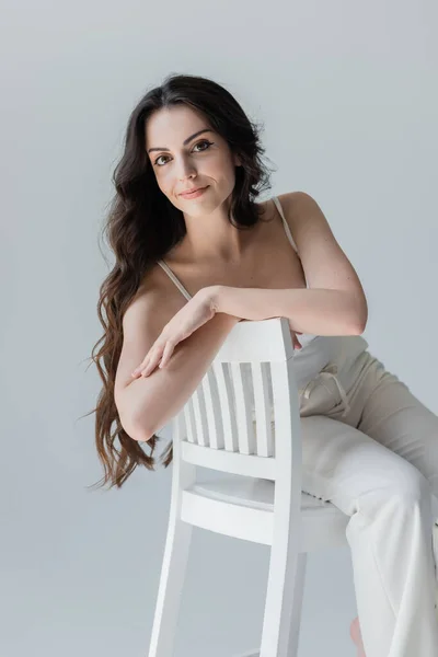 Positive long haired woman sitting on chair isolated on grey — Stockfoto