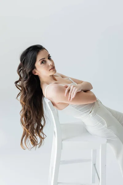 Pretty long haired woman looking at camera near chair isolated on grey — Stock Photo