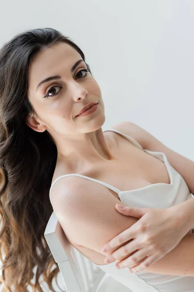 Portrait of young woman in white top posing on chair isolated on grey — Stock Photo