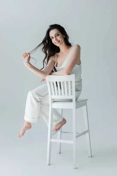 Full length of positive barefoot woman sitting on chair on grey background — Photo de stock