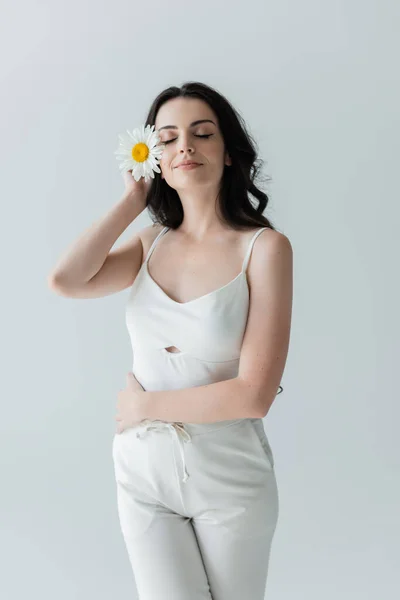 Pleased woman in white clothes holding chamomile isolated on grey — Fotografia de Stock