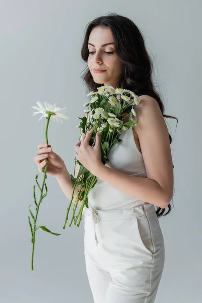 Молода модель в білому одязі, що тримає ромашки ізольовані на сірому — стокове фото