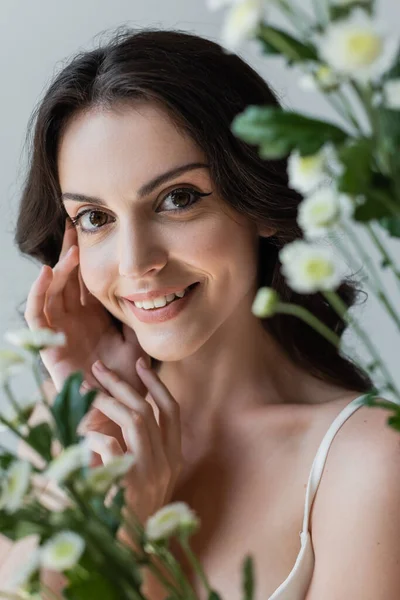 Cheerful brunette model looking at camera near blurred chamomiles isolated on grey — Stock Photo