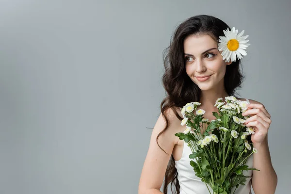 Smiling young woman holding bouquet of chamomiles isolated on grey — Stock Photo