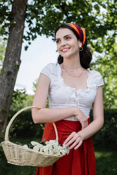 Smiling woman in blouse holding basket with flowers outdoors — Photo de stock