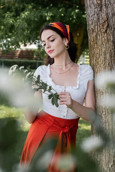 Stylish young woman in blouse holding chamomiles in park — Stock Photo
