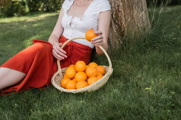 Cropped view of stylish woman holding orange near basket in park — Fotografia de Stock