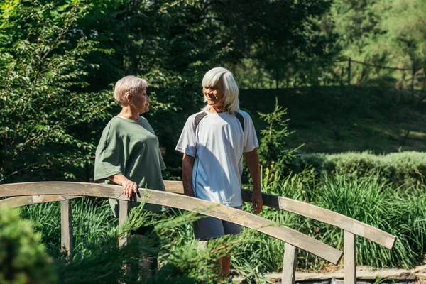 Пожилая пара в спортивной одежде, улыбающаяся стоя на мосту — стоковое фото