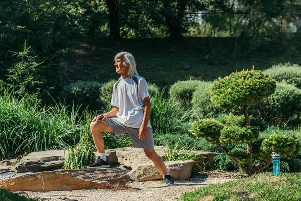 Full length of cheerful senior man with grey hair exercising in sportswear outside — Stock Photo