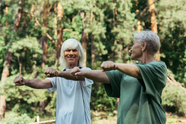 Радісна старша пара в спортивному одязі, що працює з простягнутими руками разом у парку — стокове фото