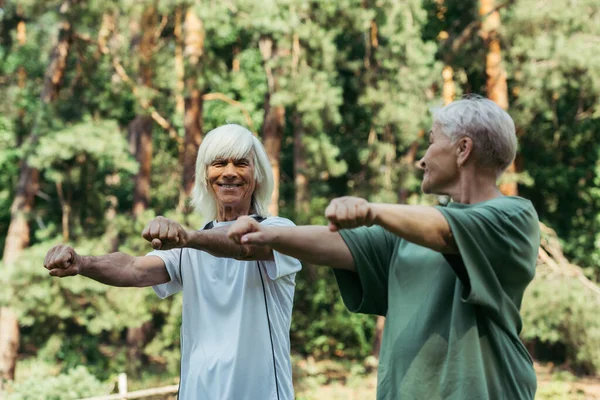 Joyful senior couple in sportswear working out with outstretched hands together in park — Foto stock