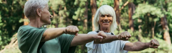 Joyful senior couple in sportswear working out with outstretched hands together in park, banner — Foto stock