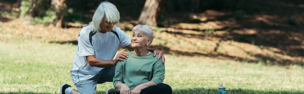 Cheerful senior man hugging wife with grey hair sitting in green park, banner — Stock Photo