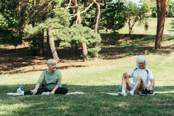 Senior woman sitting on fitness mat while looking at husband holding sneakers — Photo de stock