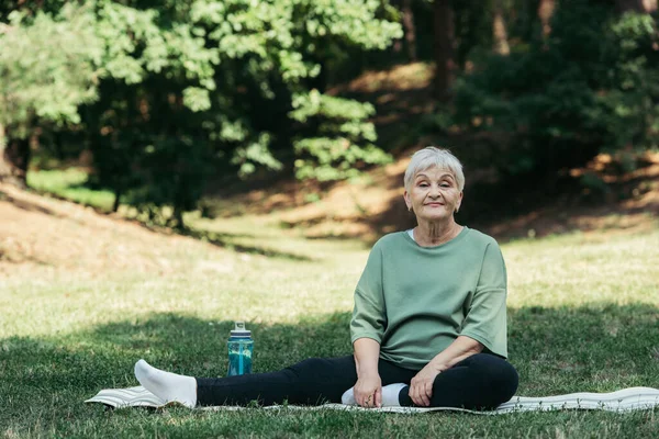 Cheerful senior woman with grey hair sitting in white socks on fitness mat — Stock Photo