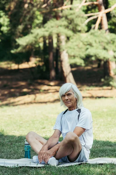 Cheerful senior man with grey hair sitting in white socks on fitness mat - foto de stock