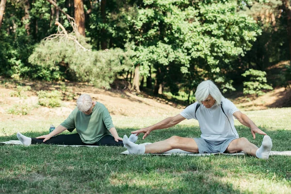 Full length of senior couple stretching while exercising on fitness mats in green park — Photo de stock