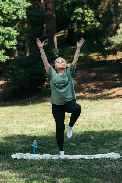 Full length of senior woman with raised hands exercising on fitness mat in park — Photo de stock