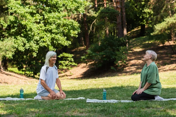 Full length of happy senior couple in sportswear sitting on fitness mats in green park — Fotografia de Stock