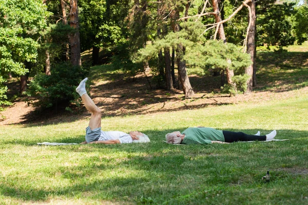 Full length of senior couple in sportswear working out on fitness mats in green park — Stockfoto