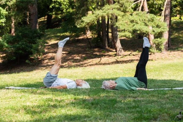 Full length of senior couple in sportswear doing shoulder stand on fitness mats in green park — Stockfoto