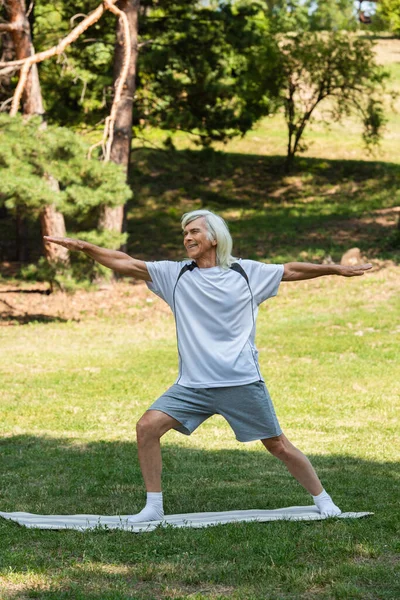 Full length of cheerful senior man with grey hair smiling and working out with outstretched hands in park — Stock Photo