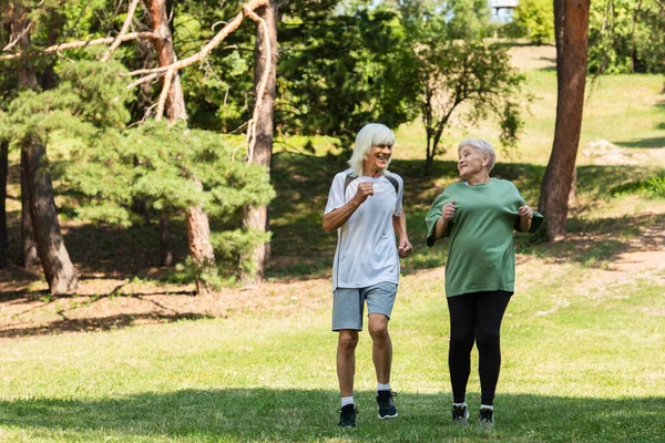 Full length of senior couple in sportswear running in green park - foto de stock