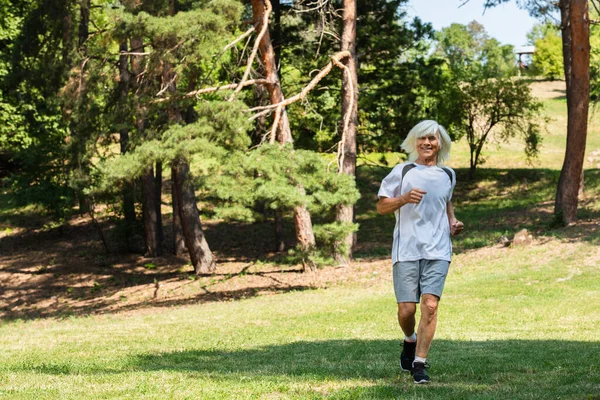 Full length of senior man in sportswear running in green park - foto de stock