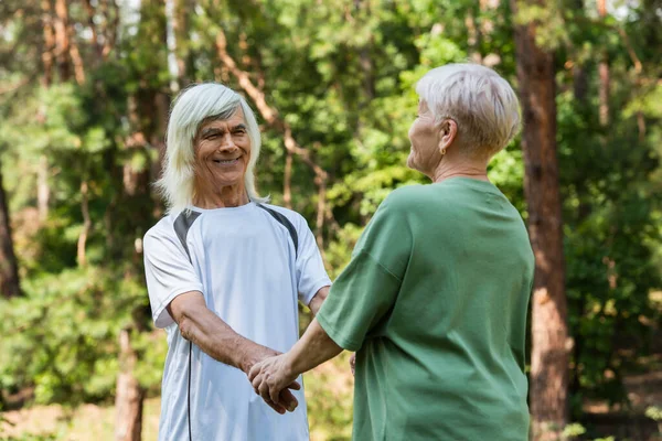 Joyful senior couple in sportswear holding hands in green park — Fotografia de Stock