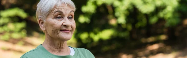 Happy and retied woman with grey hair looking away in park, banner — Stockfoto