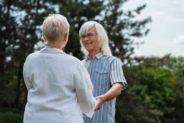 Happy senior man in glasses holding hands with wife in summer — Stockfoto