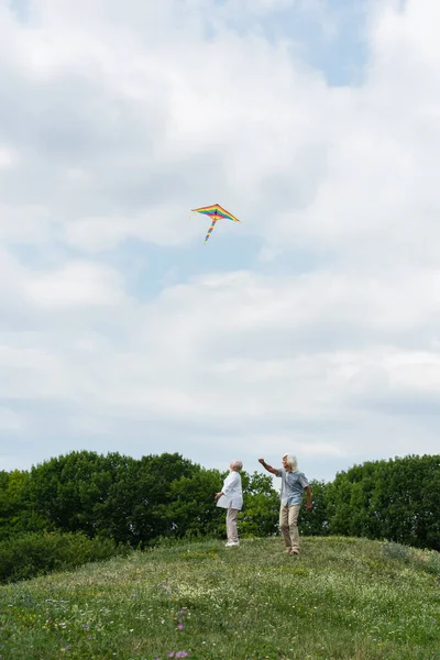 Happy senior couple in casual clothes looking at flying kite in cloudy sky — Stock Photo