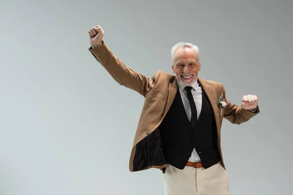 Excited middle aged groom in suit with floral boutonniere gesturing isolated on grey — Stockfoto