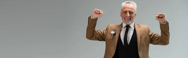 Cheerful middle aged groom in suit with floral boutonniere gesturing isolated on grey, banner — Stockfoto