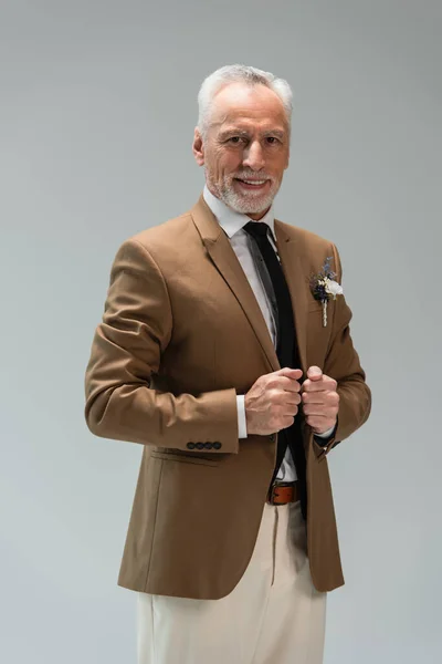 Happy middle aged groom in suit with floral boutonniere isolated on grey - foto de stock